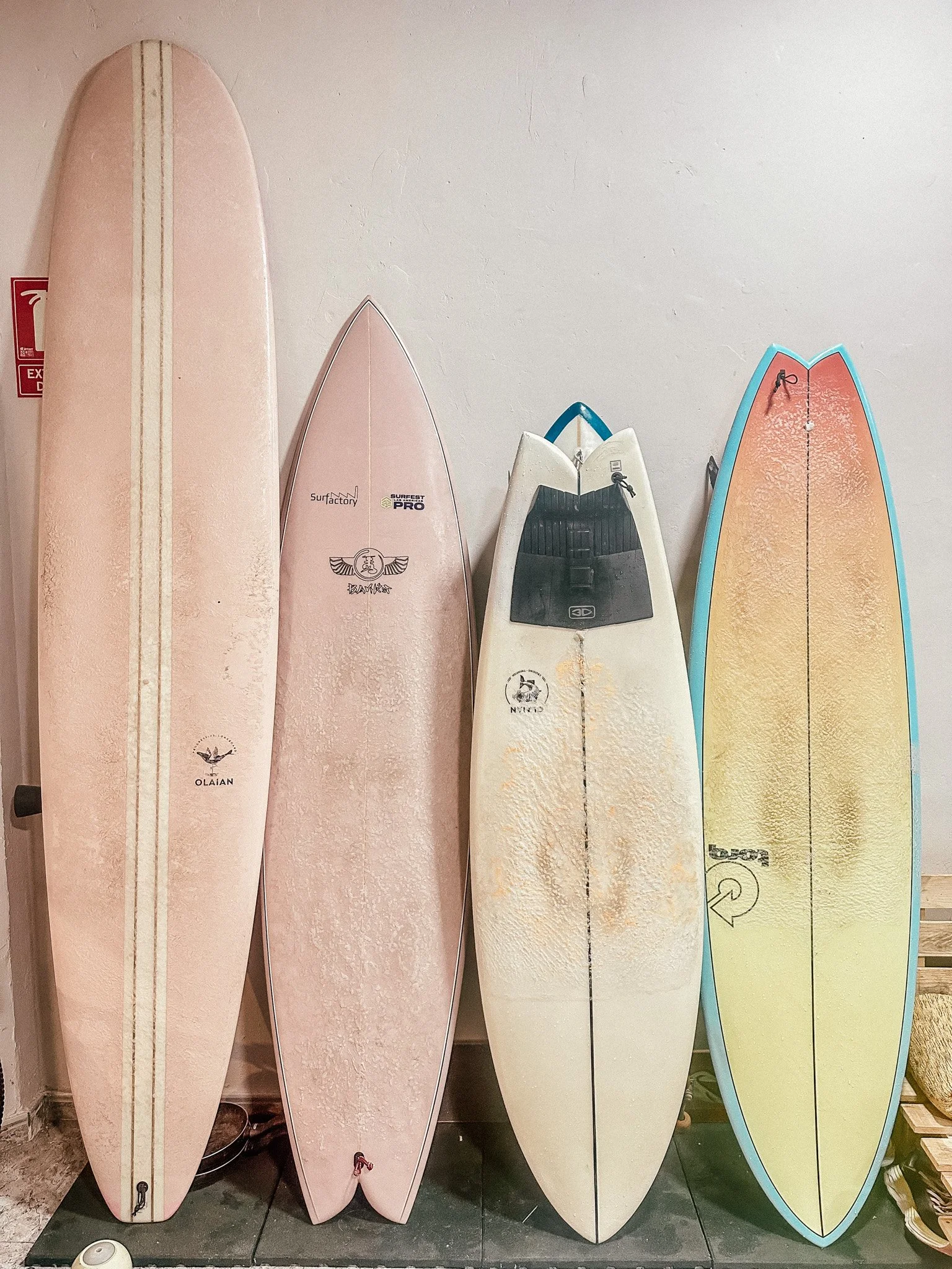 Four surfboards standing upright against a plain indoor wall.