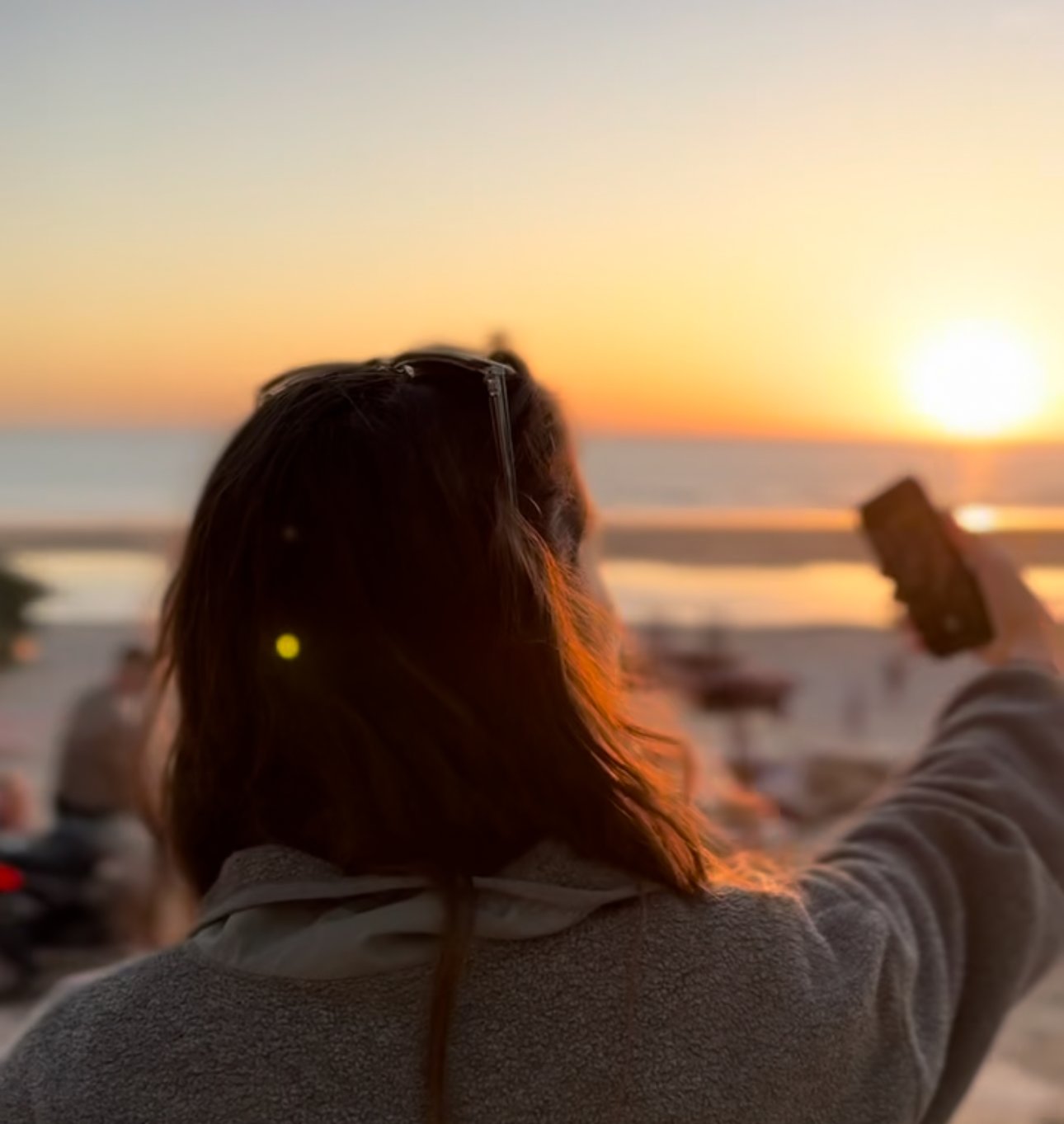 Person taking a photo with a smartphone during a beach sunset.