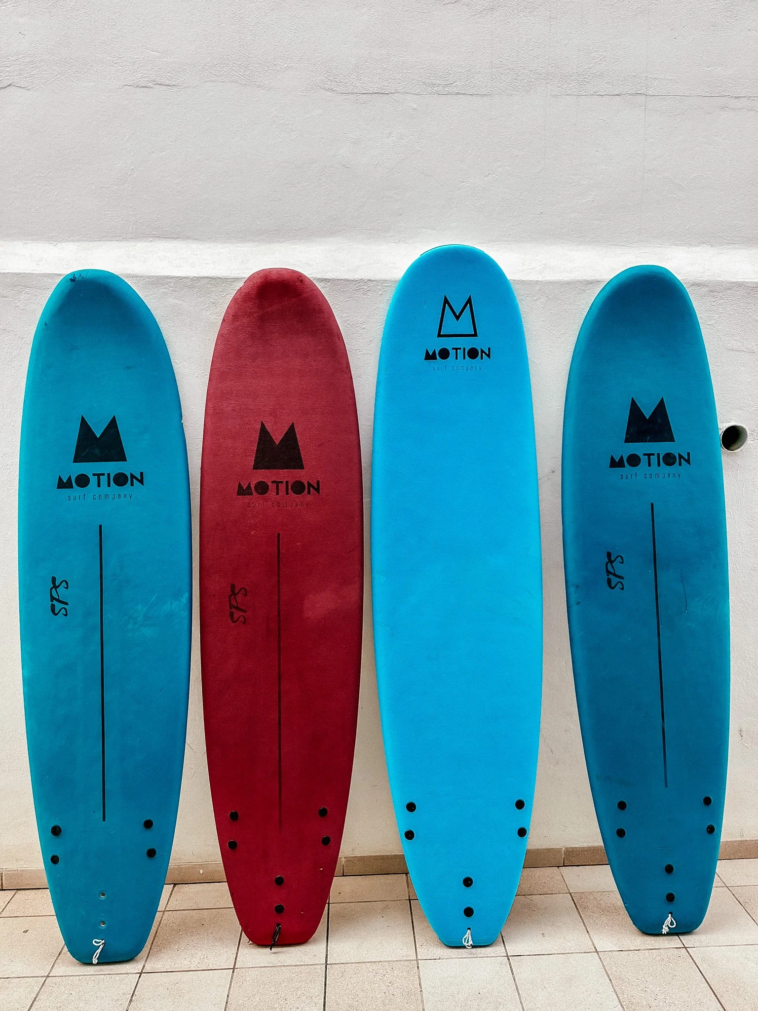 Four surfboards, two blue and two red, leaning against a white wall.