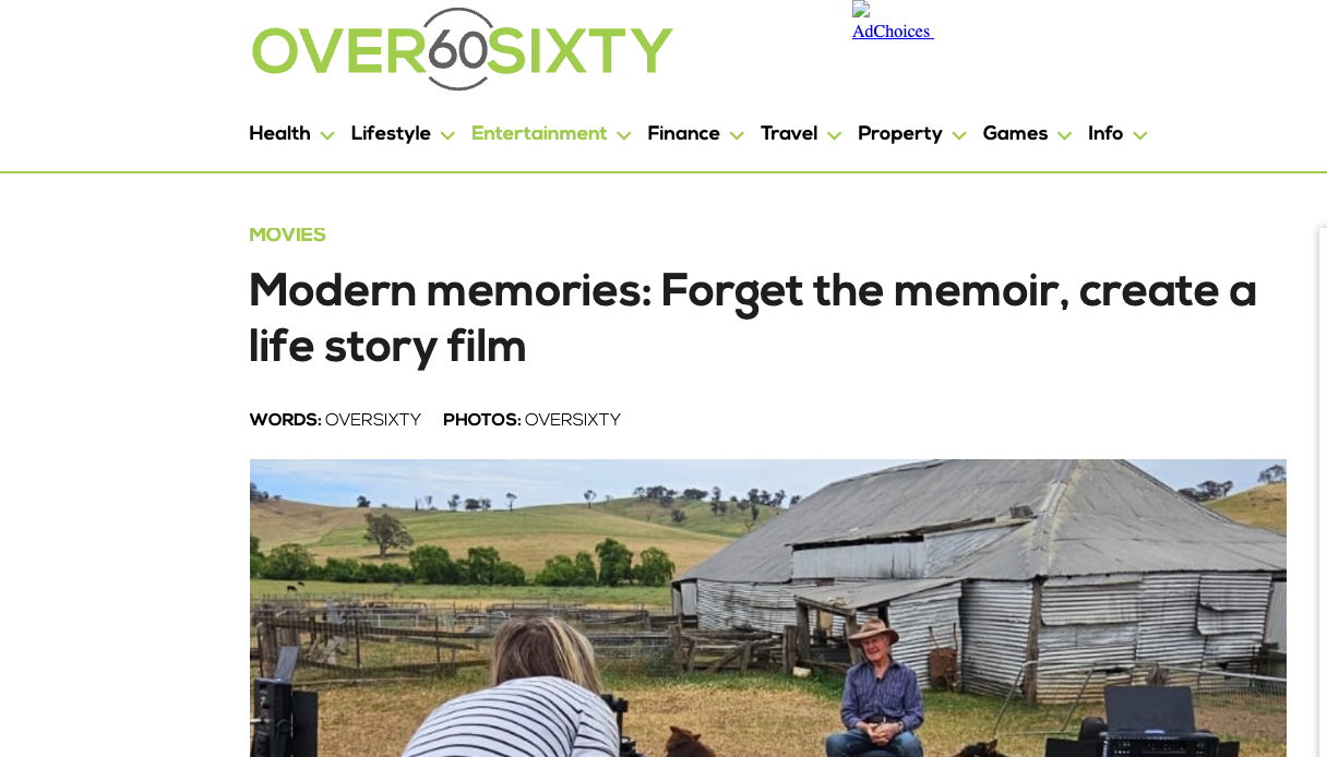 Person being photographed outdoors with a rustic barn and rolling hills in the background, during daytime.