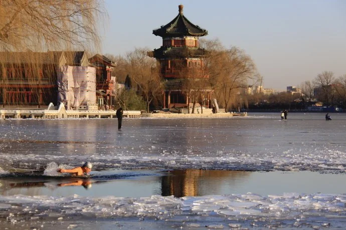 Man swimming in frozen lake in front of a temple in Beijing
