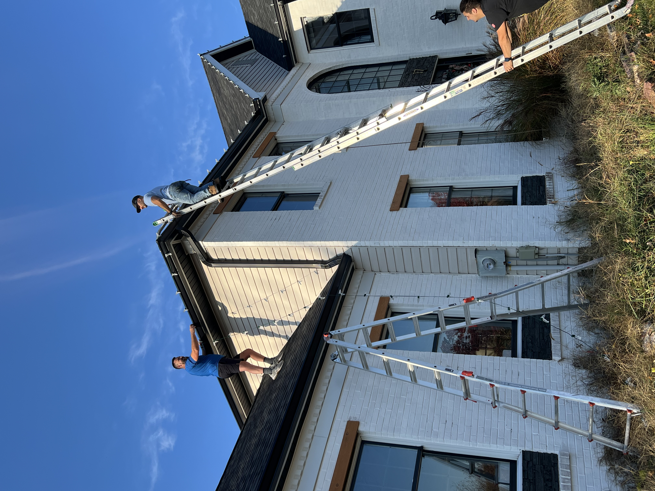 A white house with black accents house decorated with professional commercial grade Christmas light service near me. Installing Christmas lights to commercial and residential clients. 