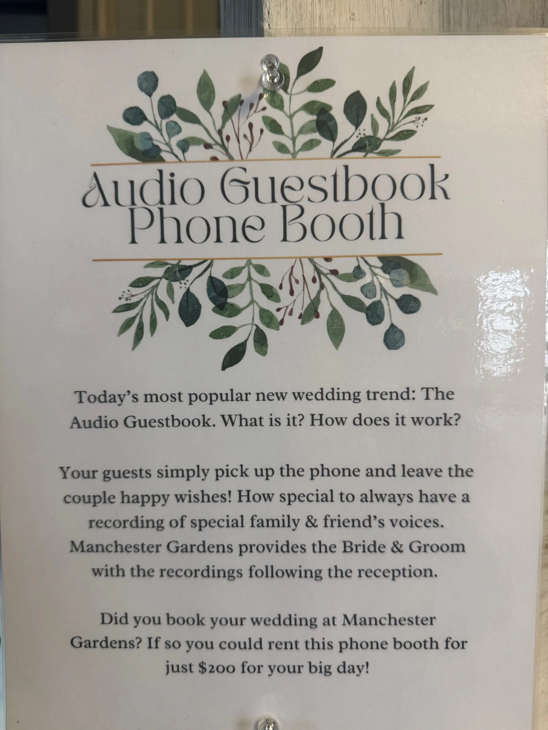 Sign at a wedding venue advertising an audio guestbook phone booth. The sign explains the concept of recording messages and mentions rental cost.
