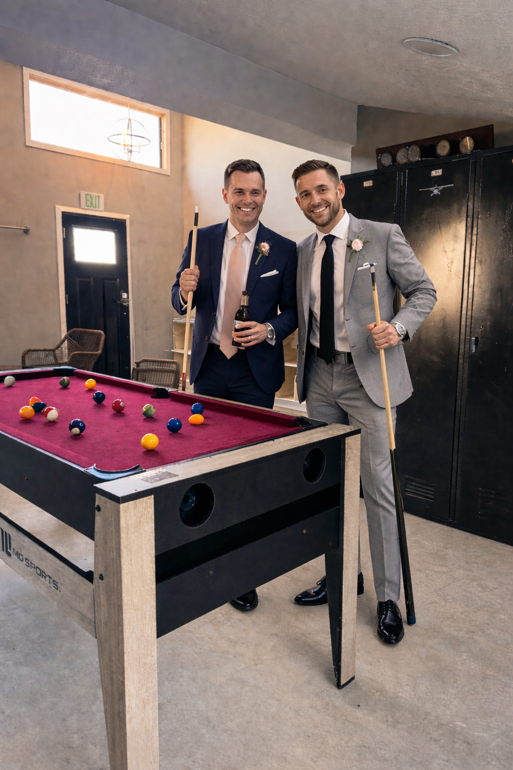 Two men in suits playing pool, smiling, with pool cues in hand, in a recreational room.