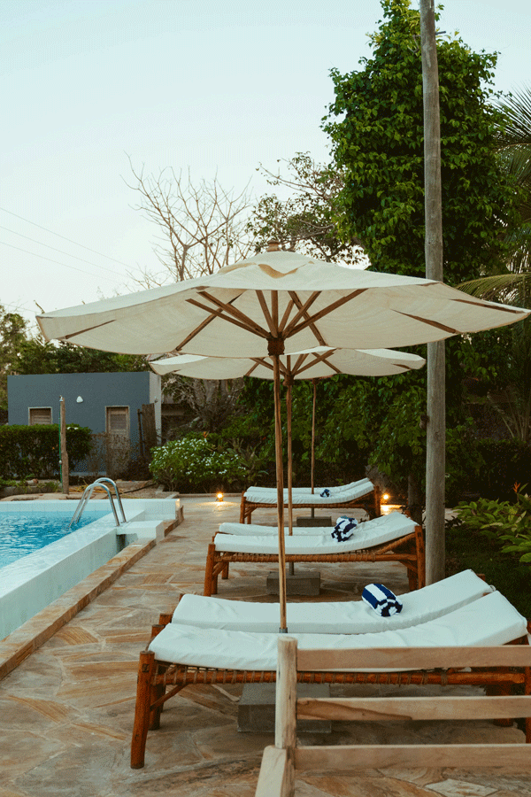 Swimming pool with lounge chairs in a lush tropical setting under a partly cloudy sky.