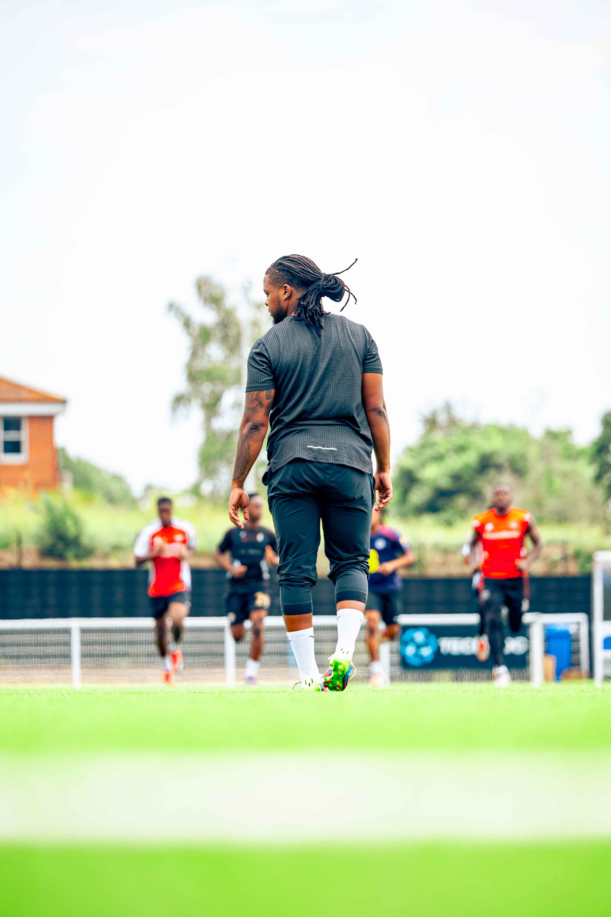 Soccer players training on a field, with a coach or player in the foreground and others running in the background