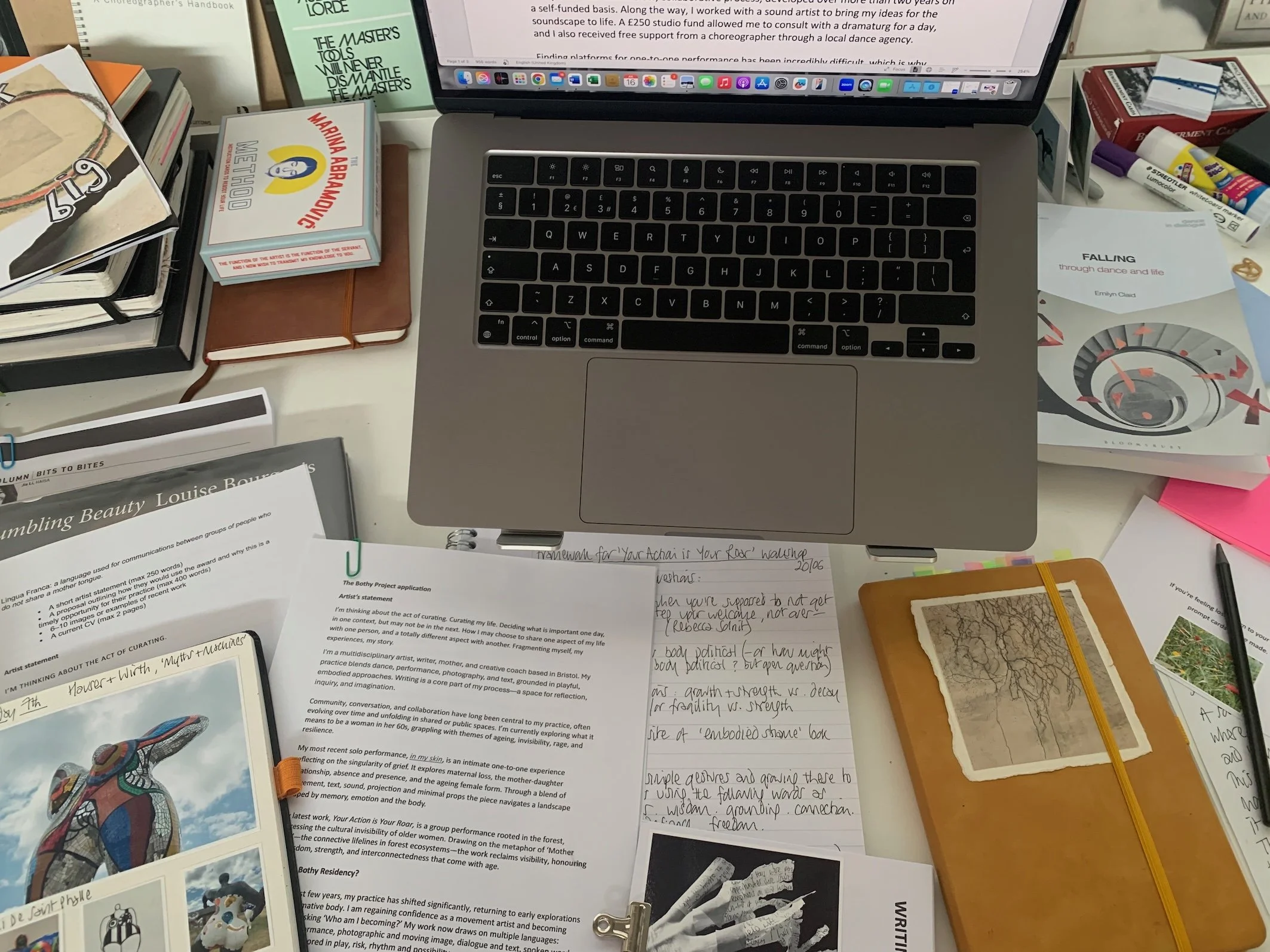Studio table showing applications, sketchbook, notebook and various publications along with an open laptop in the centre.