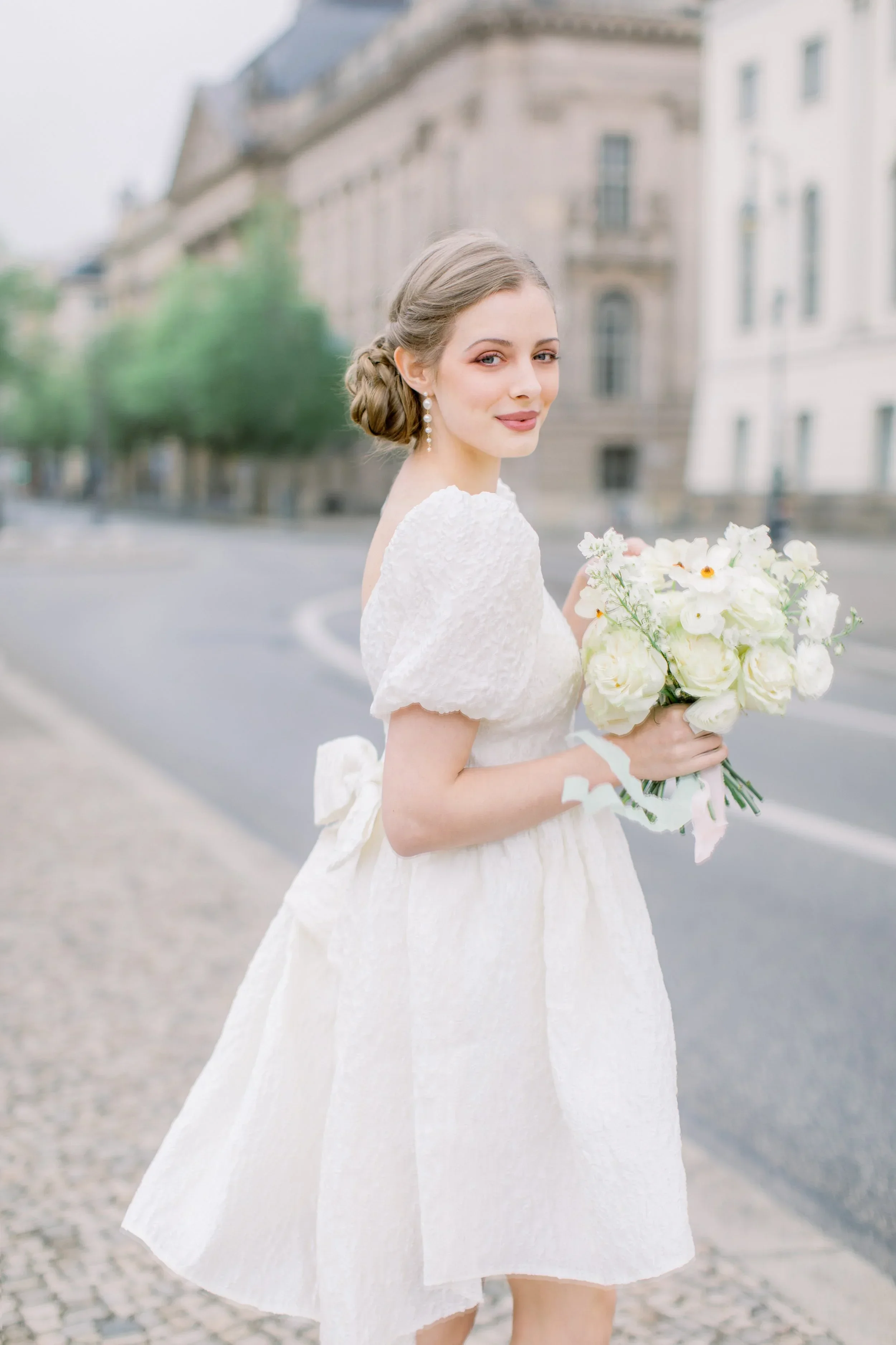 A bride wearing white holding a white wedding bouquet walking in the street of Berlin, Germany