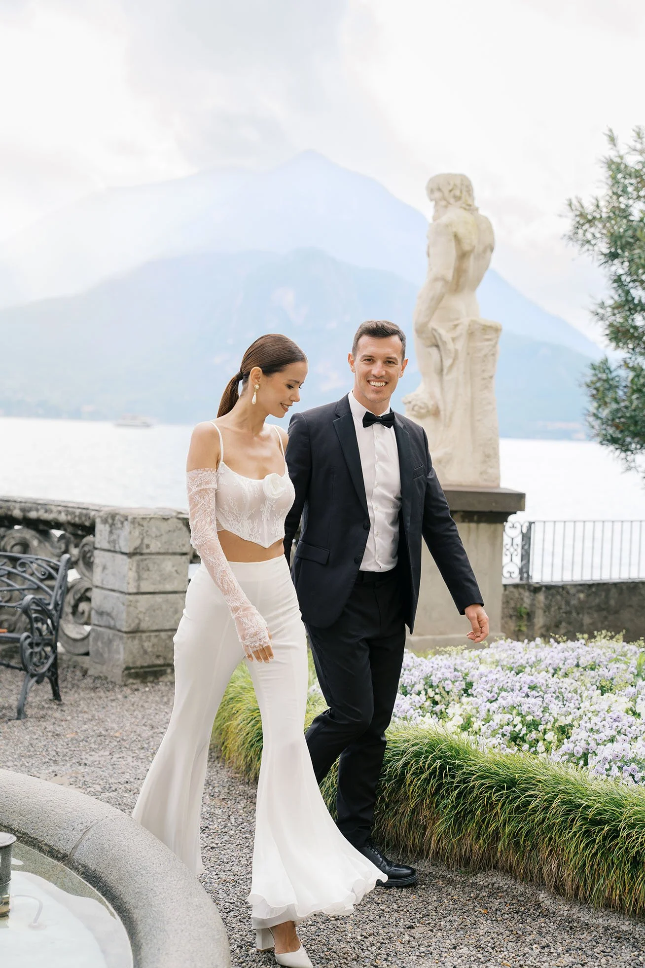 Modern wedding couple in wedding attire walking and smiling to the camera at Villa Monastero garden.