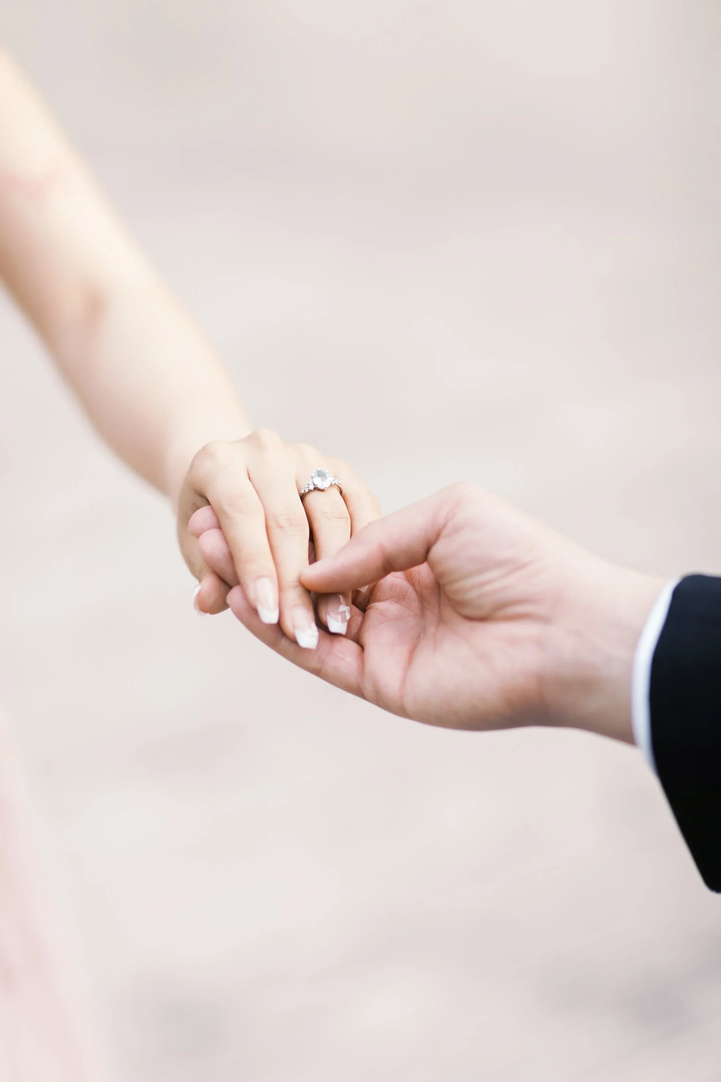 A groom holding the hand of a bride, with a close-up on her engagement ring.