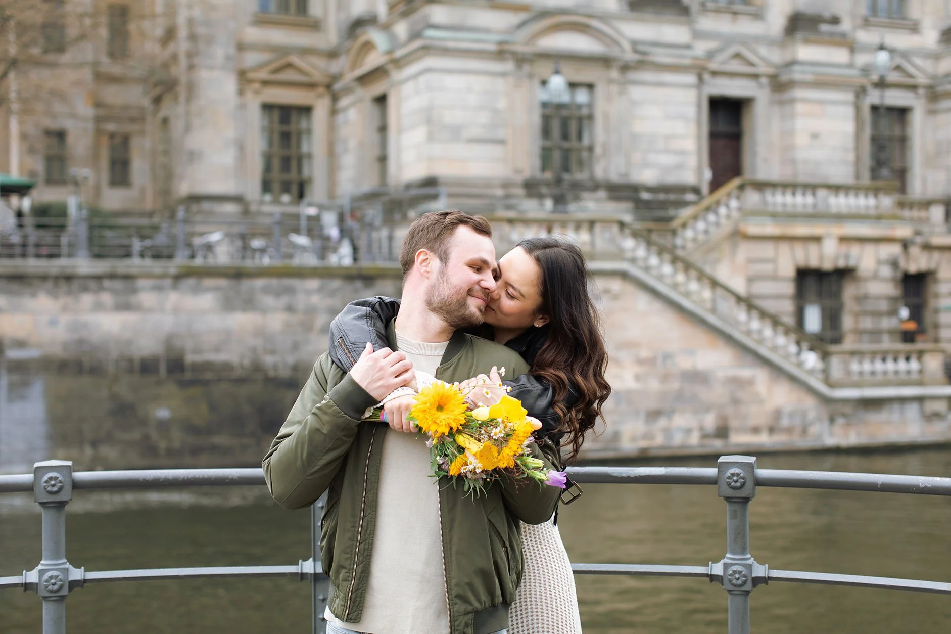 Romantic Berlin photoshoot location with an engaged couple holding flowers by the river.