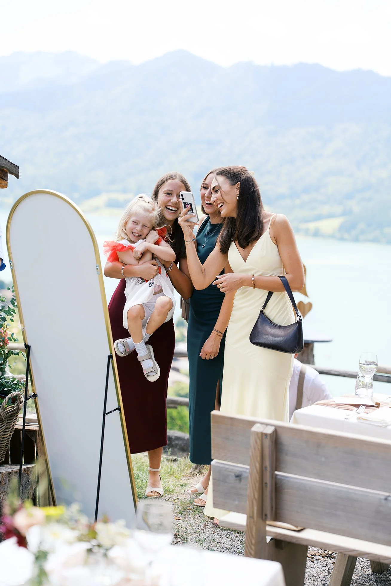 A candid photo of a group of sisters laughing and taking a selfie in front of a mirror at a wedding celebration.