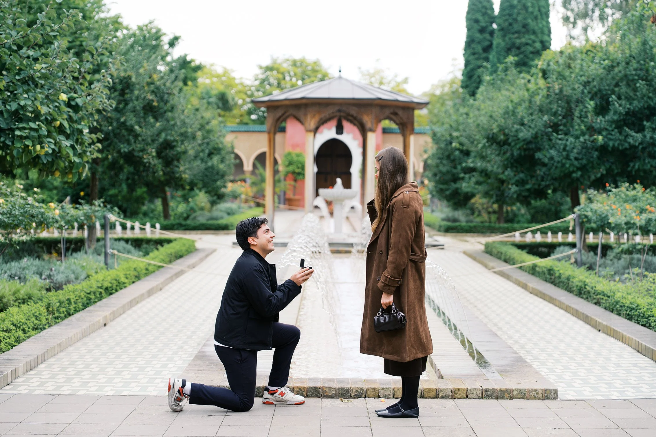 Man getting down on one knee to propose to his girlfriend in a beautiful garden in Berlin.