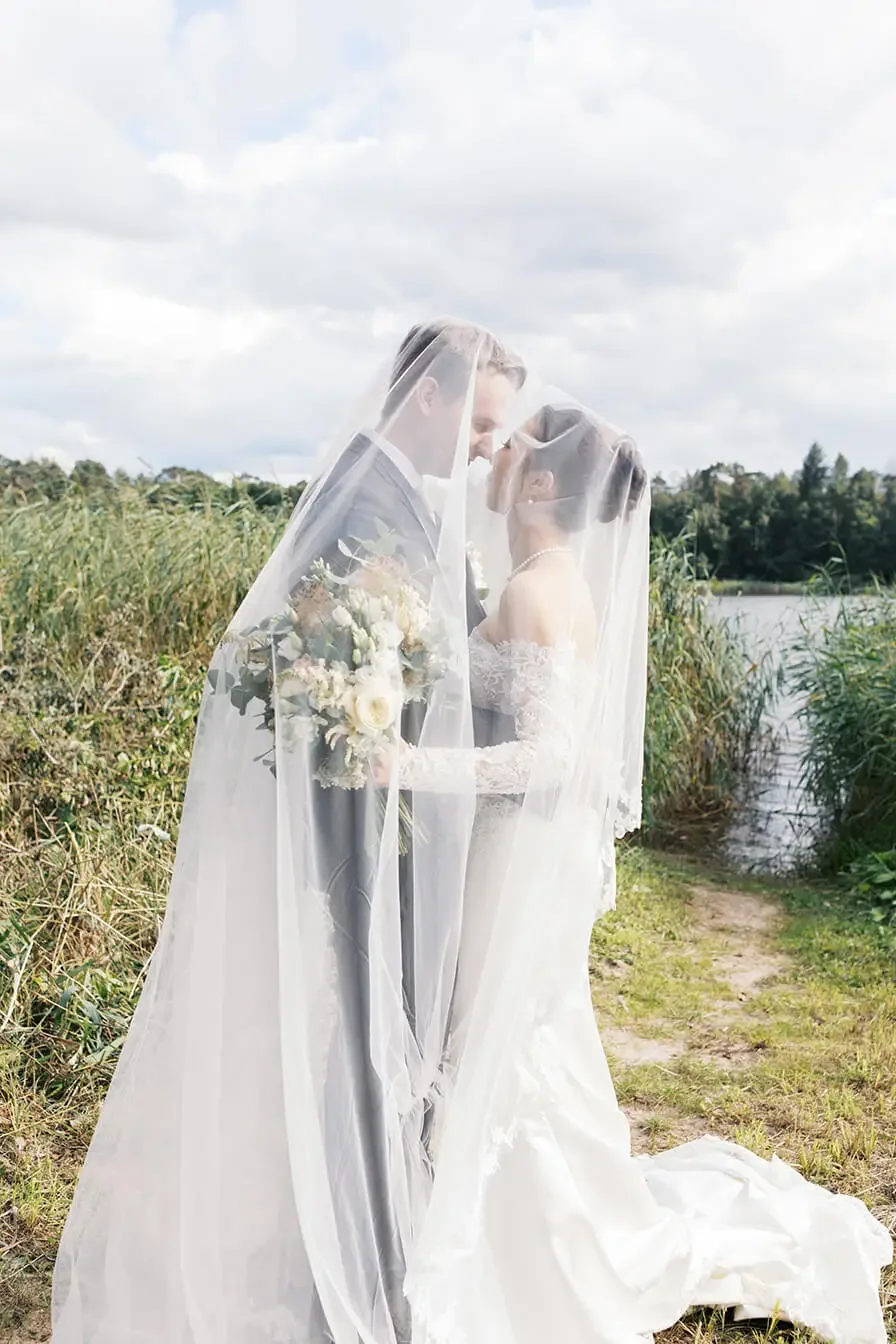 Married couple embracing each other under a veil, they are standing in the nature.