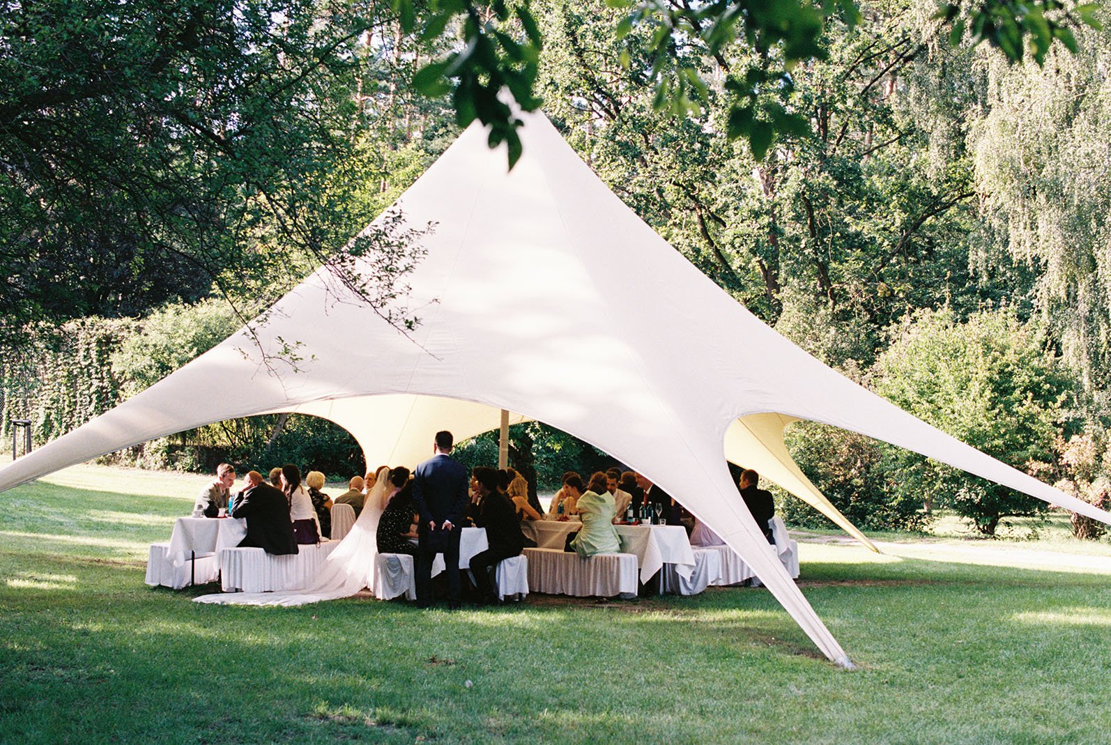 Wedding reception under a big tent on the grass with wedding couple and guests in Berlin.