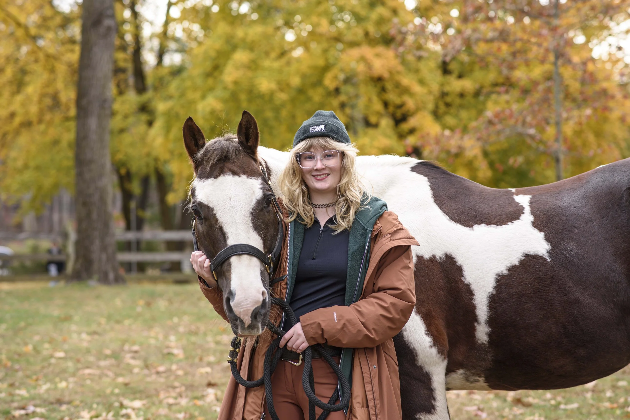 A young woman stands in front of a white and brown horse