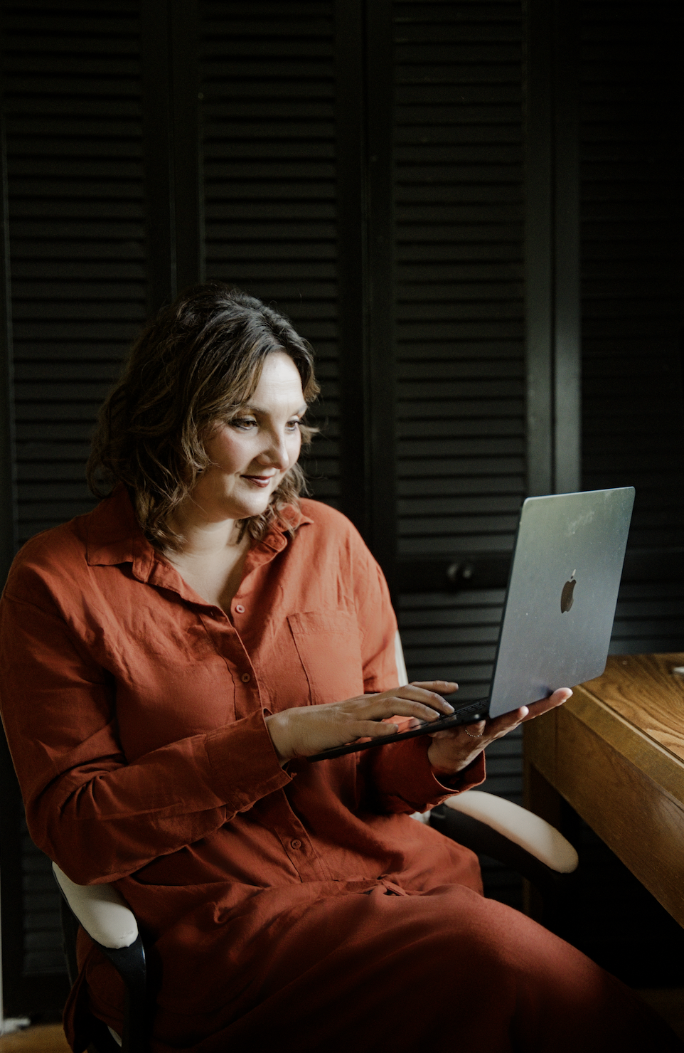 Woman wearing an orange shirt using a laptop in a dimly lit room.