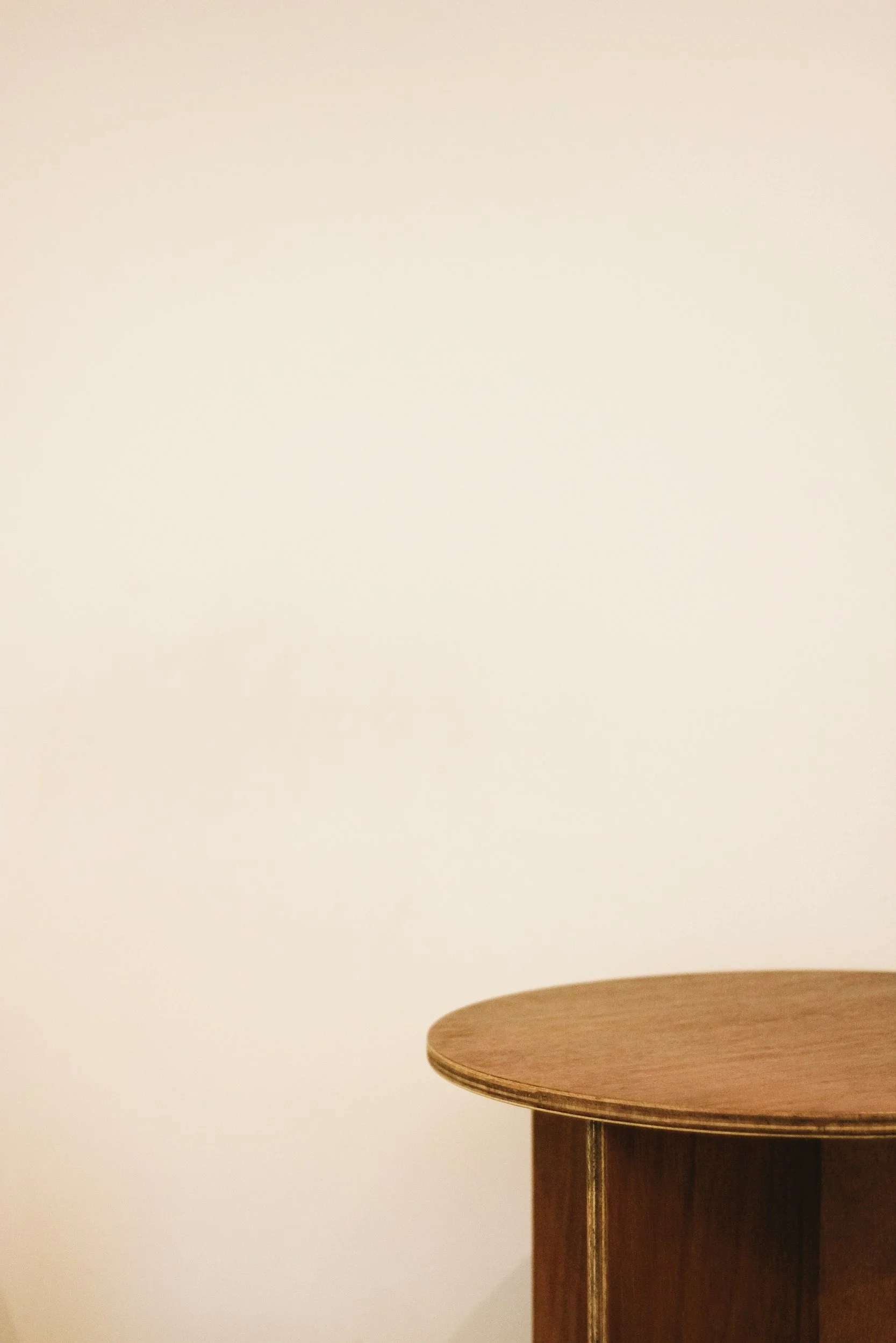 Close-up of a round wooden table against a plain white wall.