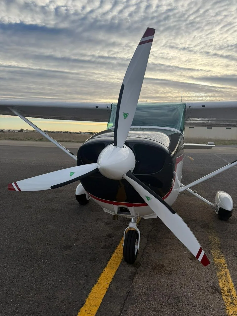 Ein einzelnes kleines Propellerflugzeug steht auf einer Startbahn Blick auf den Propeller. Der Himmel ist bewölkt, die Sonne ist untergegangen oder aufgegangen.