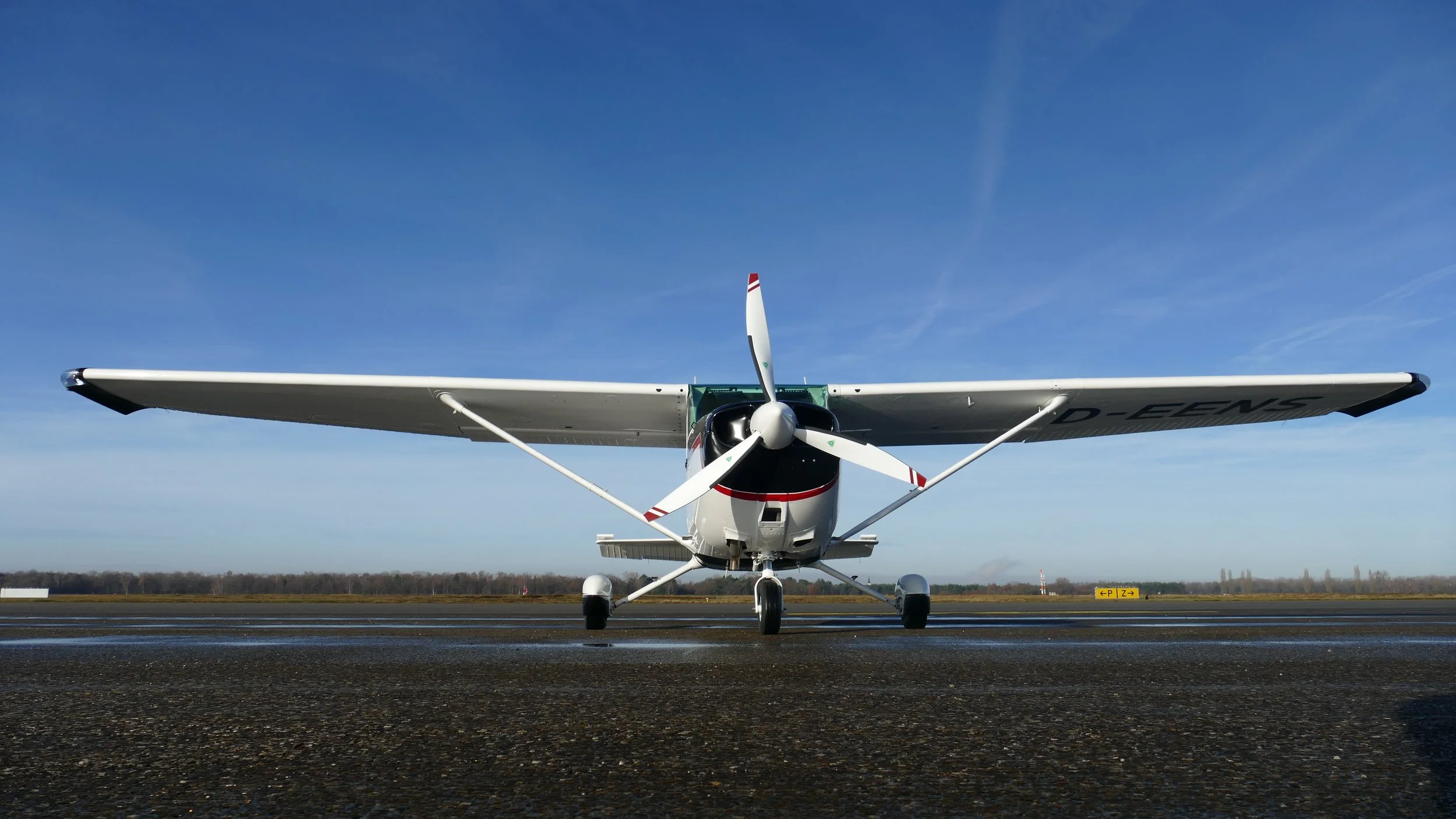 Weiß-Schwarz-Rotes Flugzeug auf dem Flugplatz, Blick frontal auf das Flugzeug, blauer Himmel, flache Landschaft im Hintergrund.