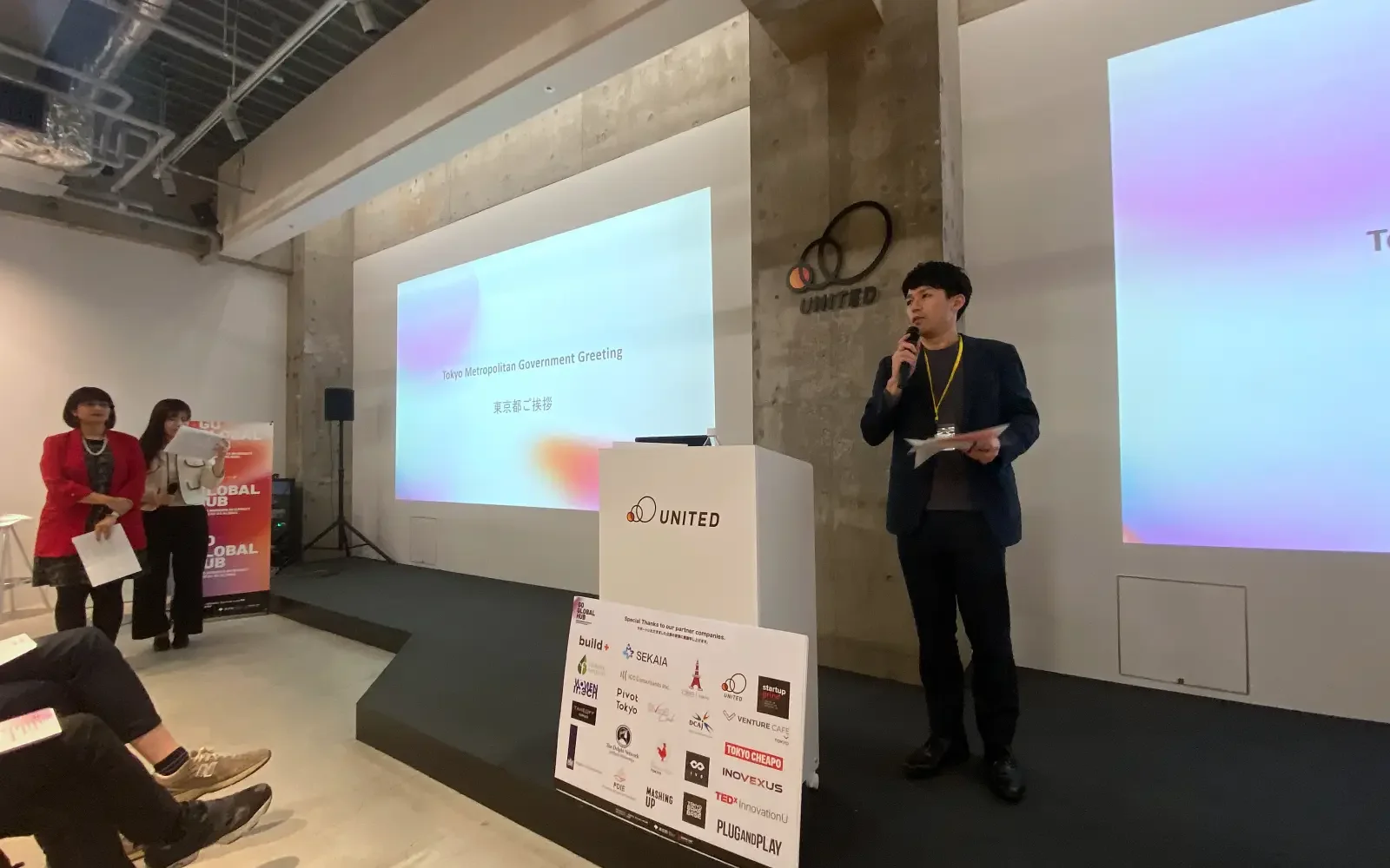 A representative from the Tokyo Metropolitan Government delivers a greeting at the Global Connector Salon, emphasizing public support for the Startup Ecosystem with sponsorship branding visible on the podium.