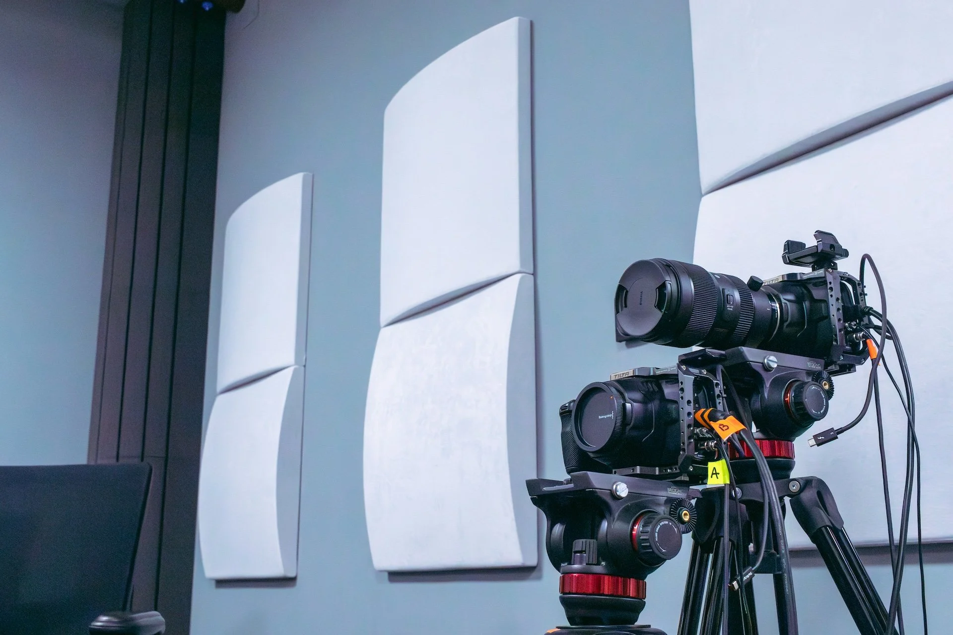 Professional camera equipment set up in front of curved acoustic panels mounted on a wall, capturing an indoor environment with soft lighting