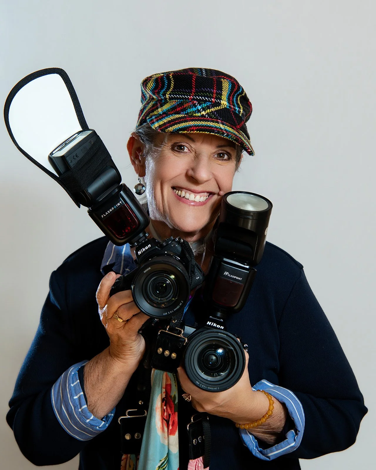 Woman holding camera lenses against pink background, smiling.