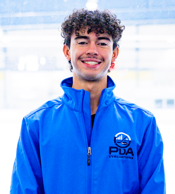 Young man with curly dark hair smiling, wearing a black shirt, standing against a plain white wall.