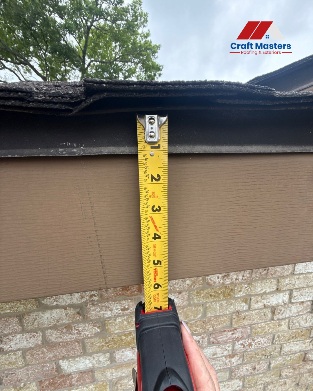 Measuring roof edge clearance with a tape measure beneath asphalt shingles above exterior siding.