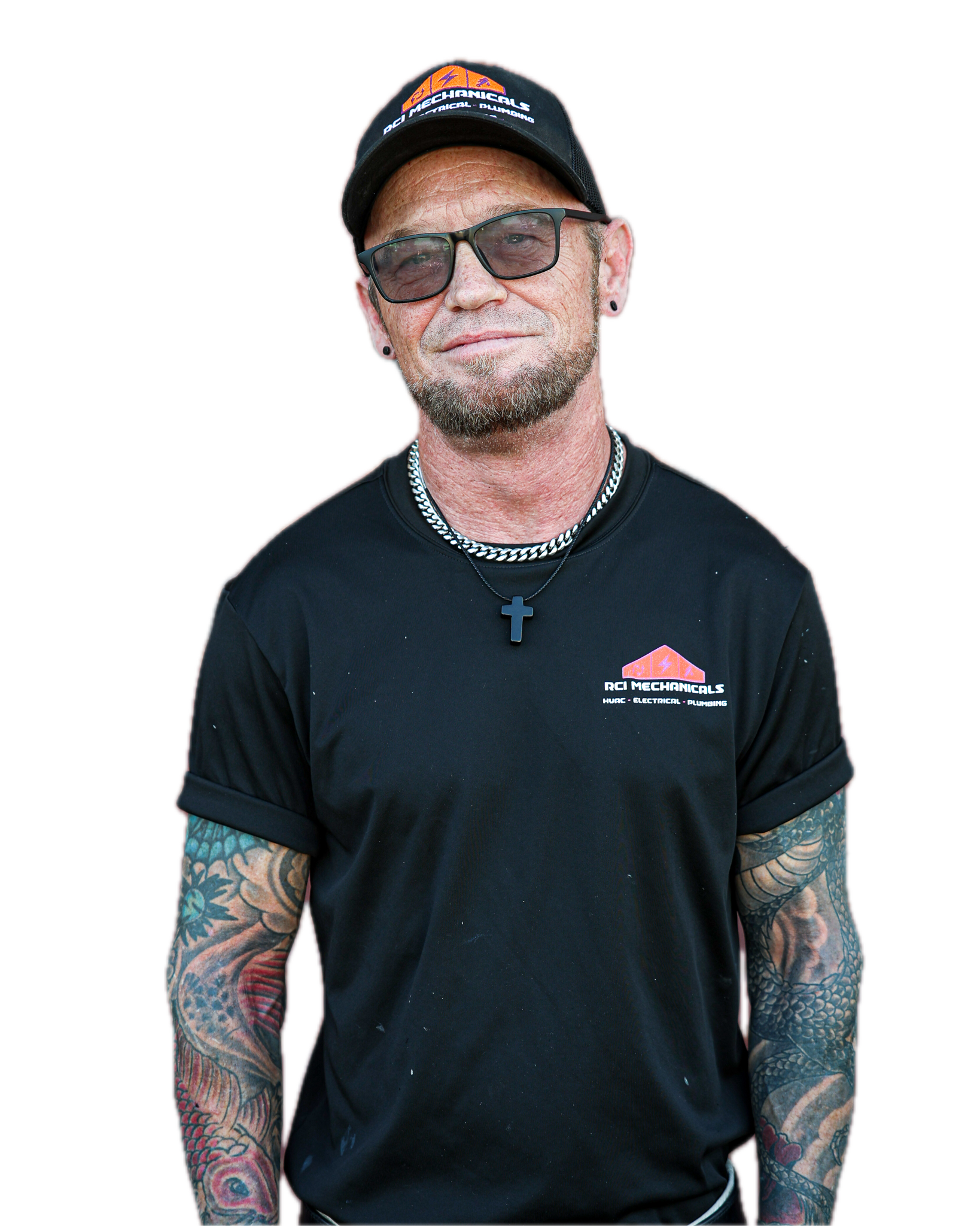 A man with glasses, tattoos on his arms, and a goatee beard is wearing a black cap and a black T-shirt with a logo and text on it. He is also wearing a necklace with a cross pendant.