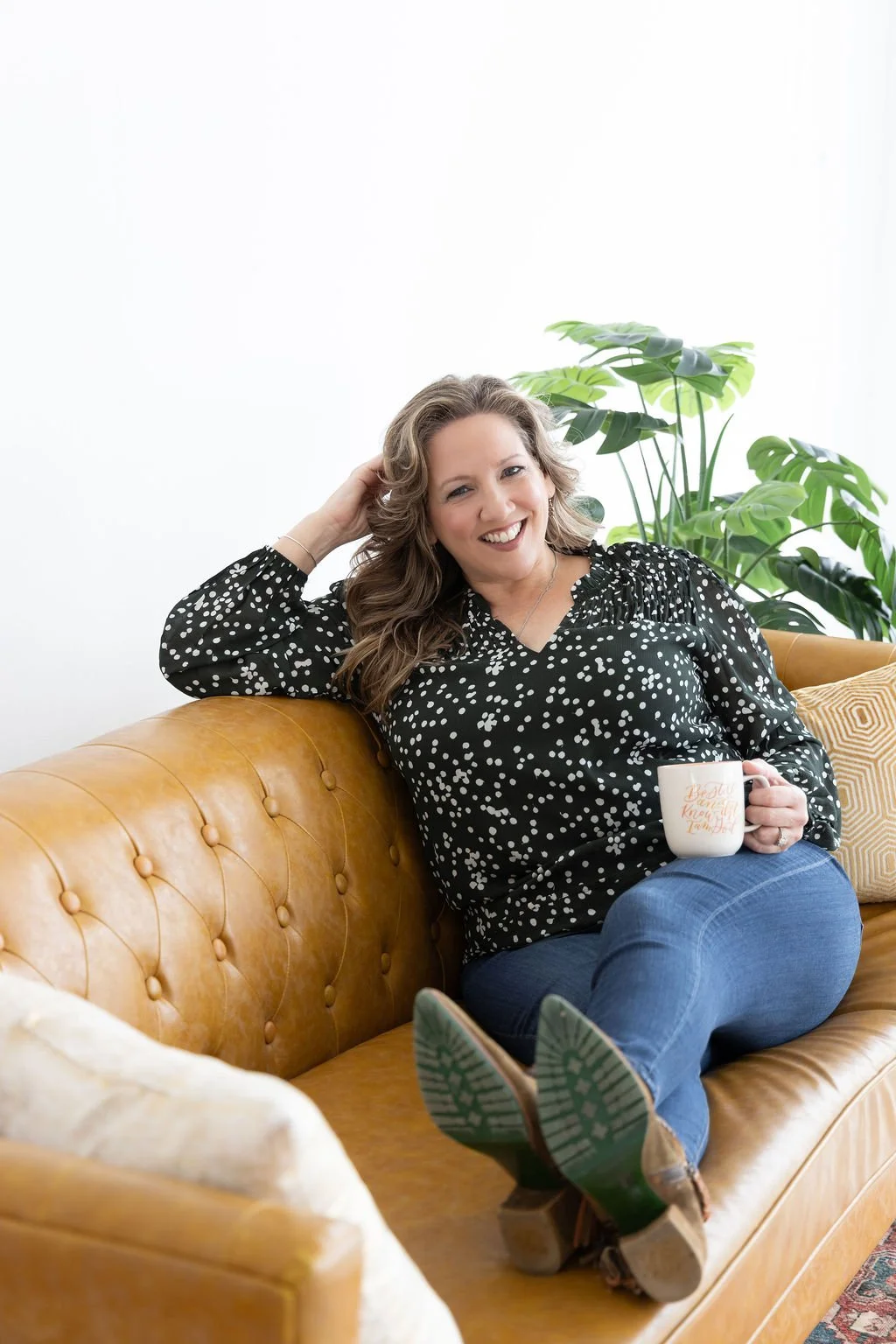 A counselor sits on a couch holding a cup of tea while providing therapy for life transitions.