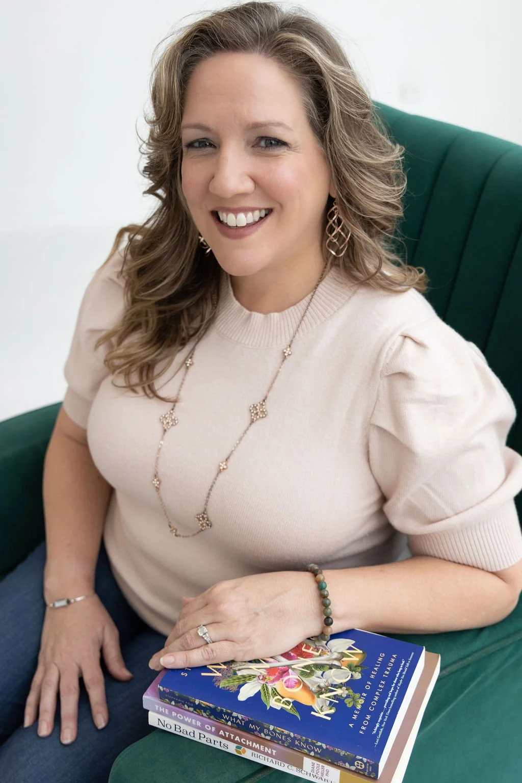 A Plano therapist sits on a chair holding books that focus on trauma-informed care.