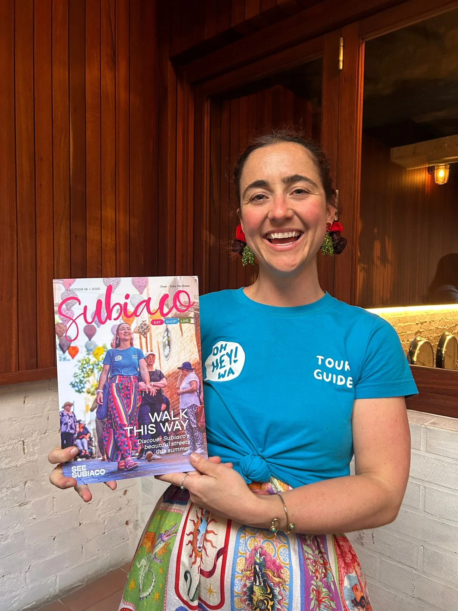 Adie smiles and holds a copy of the Subiaco magazine. She is also pictured on the cover.