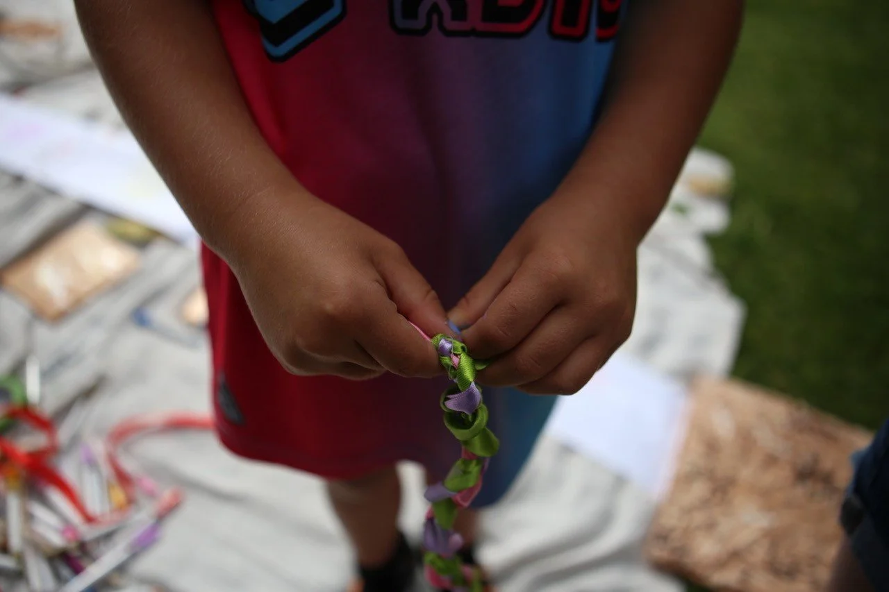 Child holding a colorful braided bracelet with purple and green ribbons.