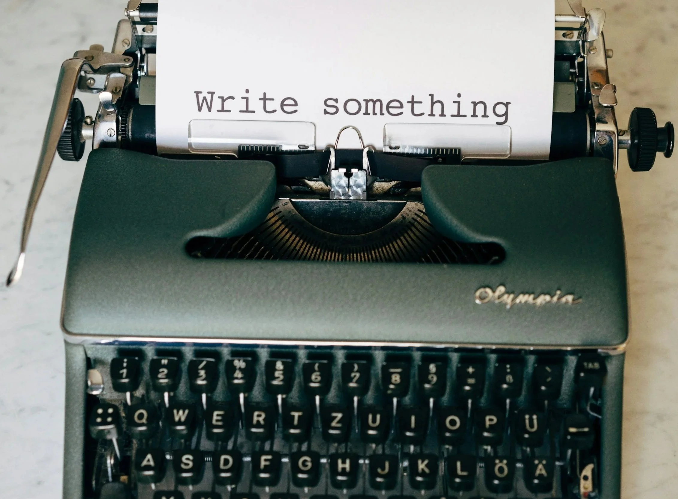 Typewriter with paper reading the words 'Write something" on it.