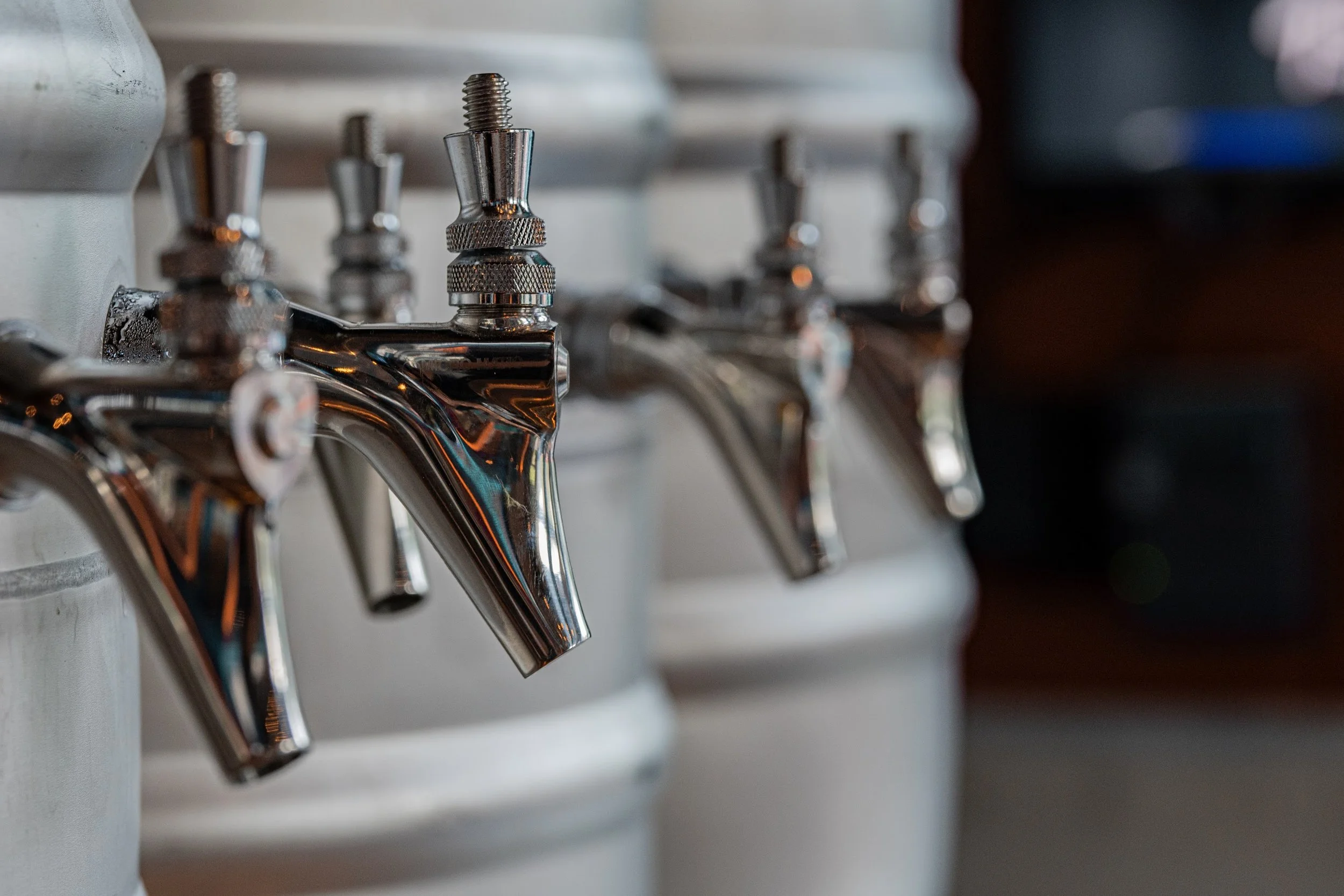 Close-up of metallic faucets with a shiny chrome finish, mounted on a white surface, likely in a bathroom or kitchen.