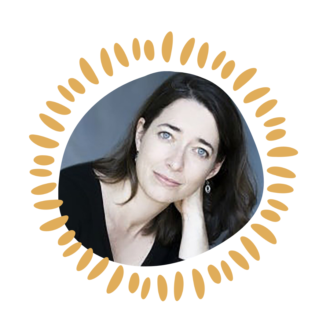 A woman with dark hair and blue eyes, wearing earrings, resting her chin on her hand and looking at the camera.