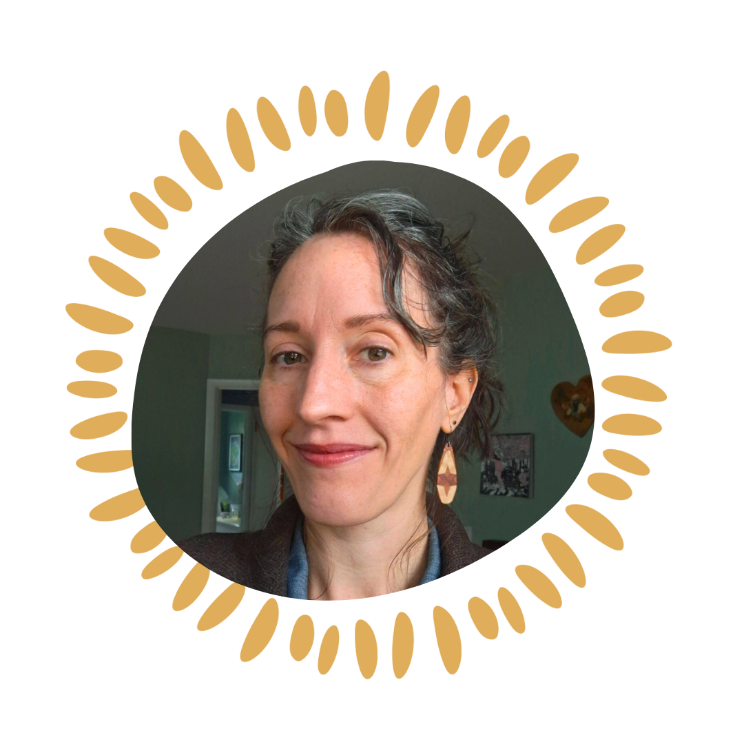 A woman with dark curly hair and earrings smiling at the camera, inside a room with green walls and a doorway in the background.
