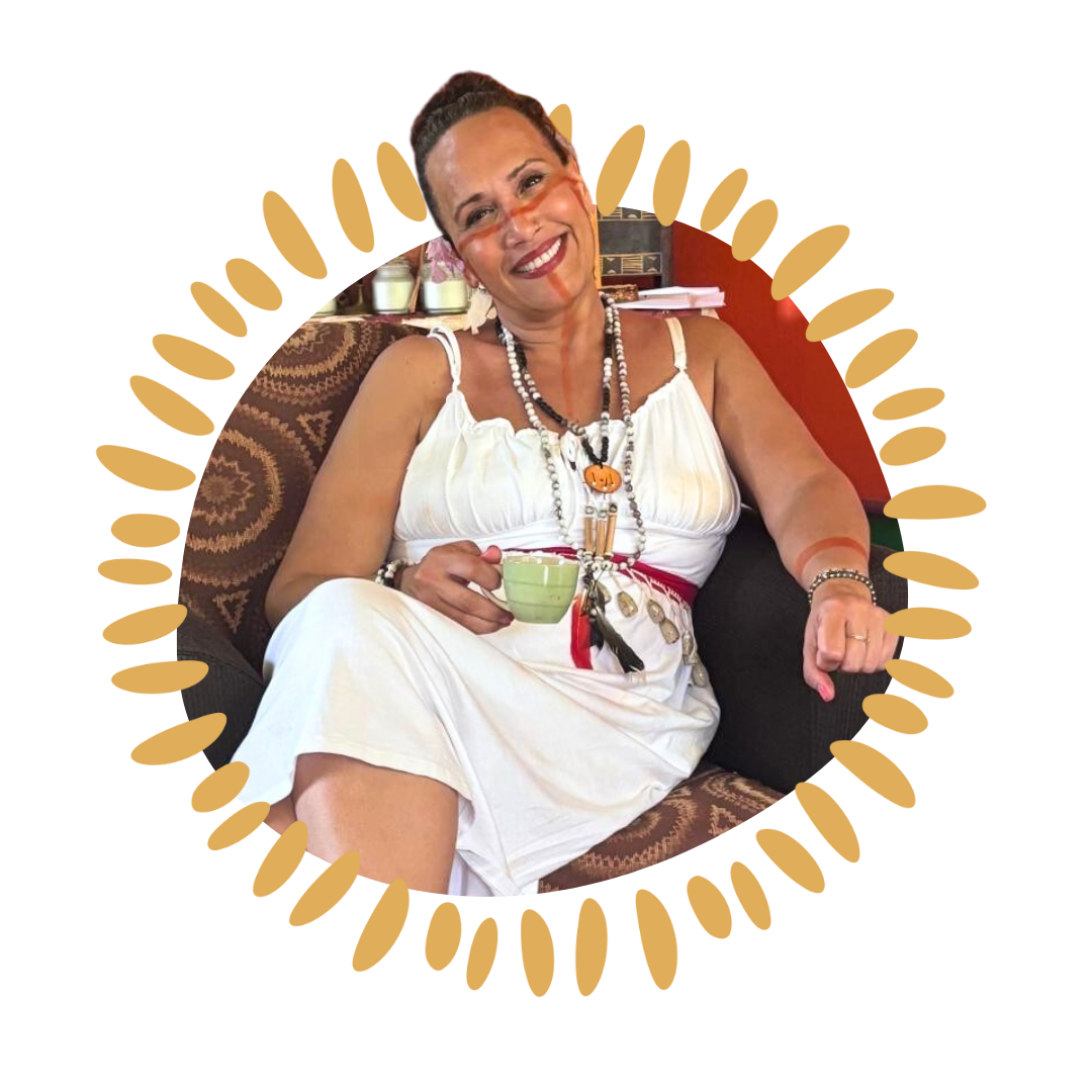 Smiling woman sitting on a chair, holding a cup, wearing a white dress and jewelry.