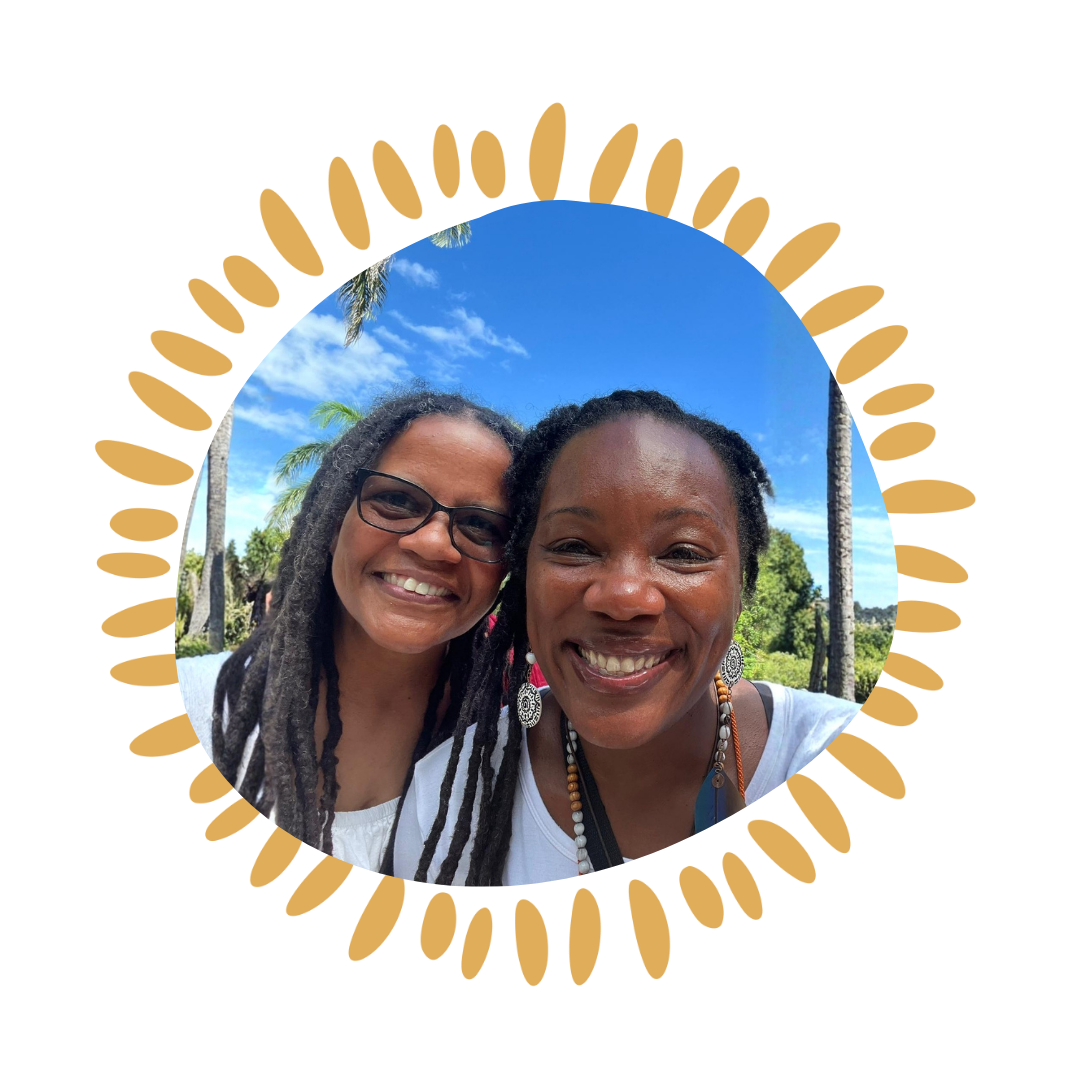 Two women smiling outdoors, with palm trees and a blue sky with clouds in the background.