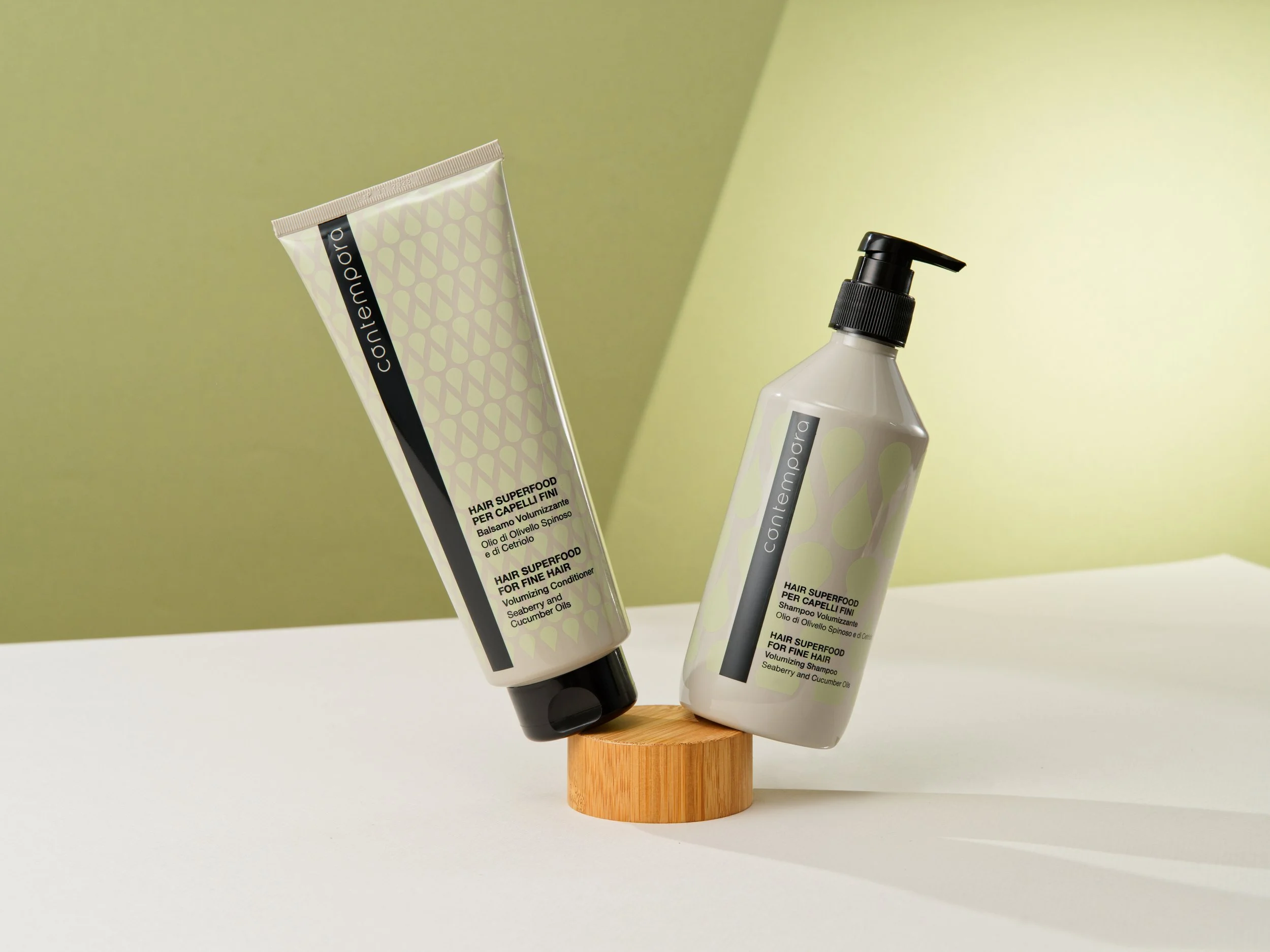 Two hair care products, a tube and a pump bottle, labeled 'Contemporia', positioned on a small wooden stand against a green and white background.