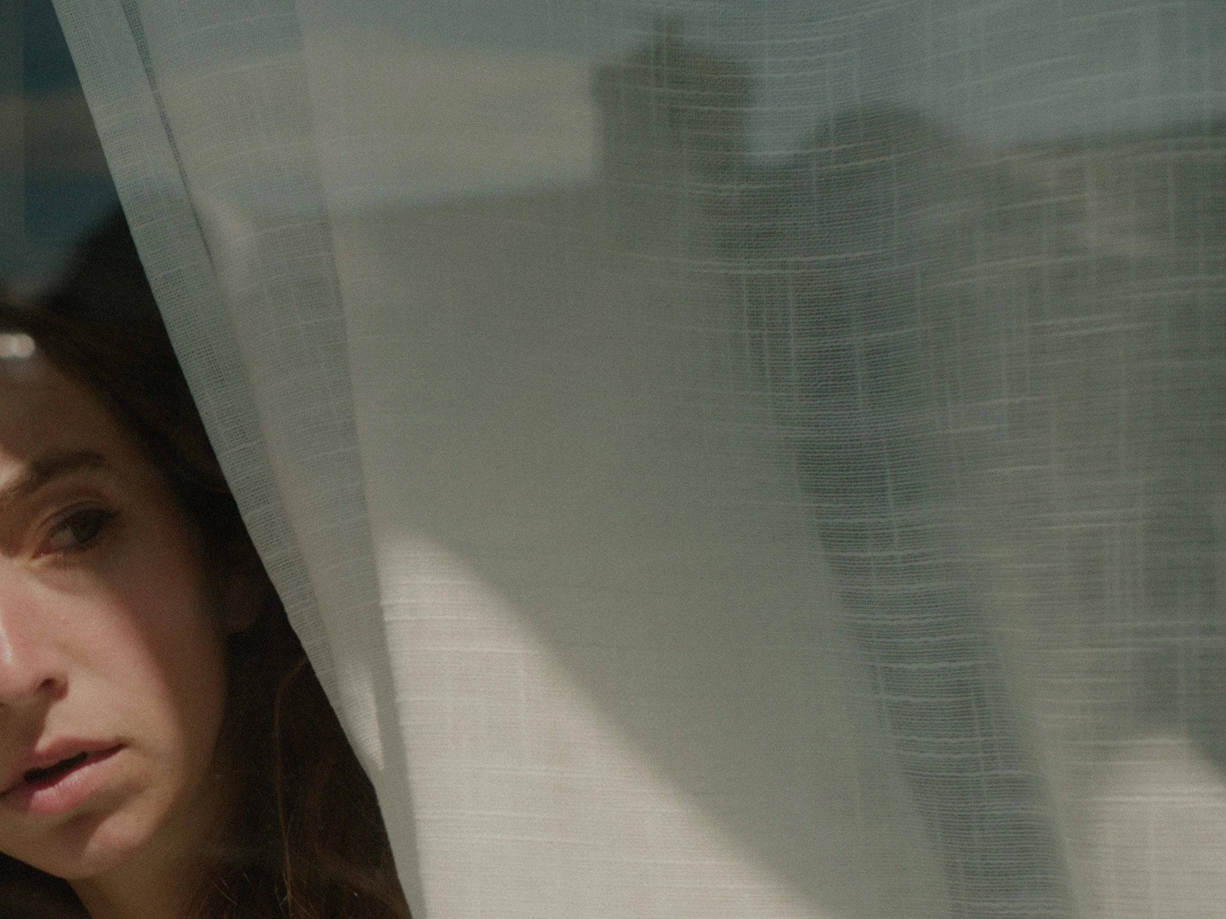A woman looking out a window through the curtains.