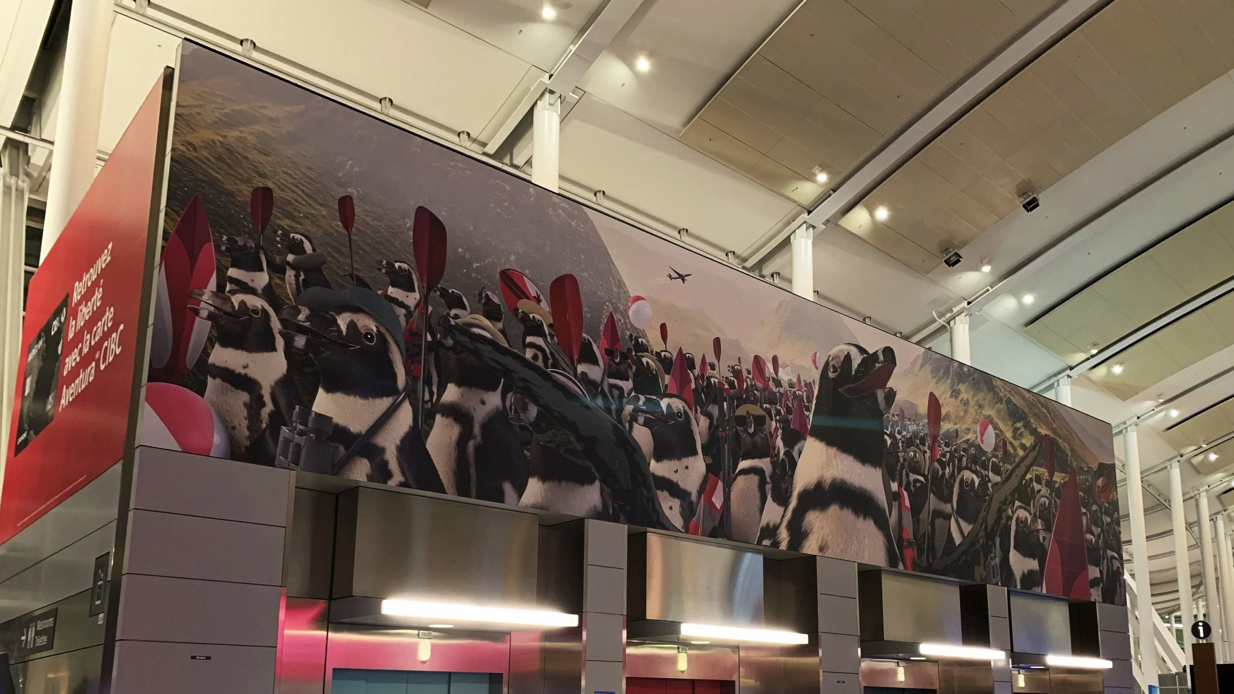 A billboard showing an army of penguins, above a bank of elevators..