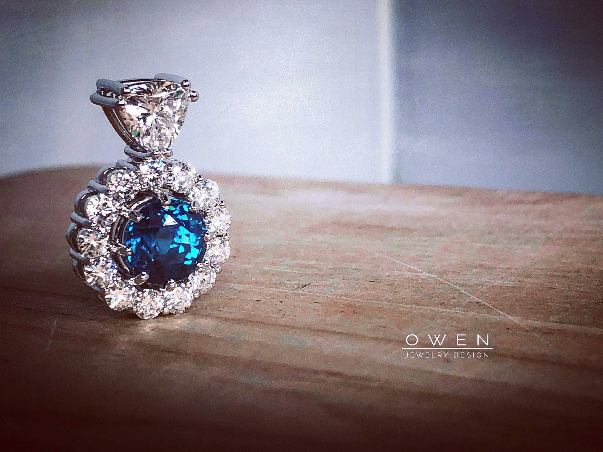 CUSTOM WHITE GOLD PENDANT WITH BLUE ZIRCON, A TRILLION CUT DIAMOND, AND A HALO OF ROUND DIAMONDS.jpg