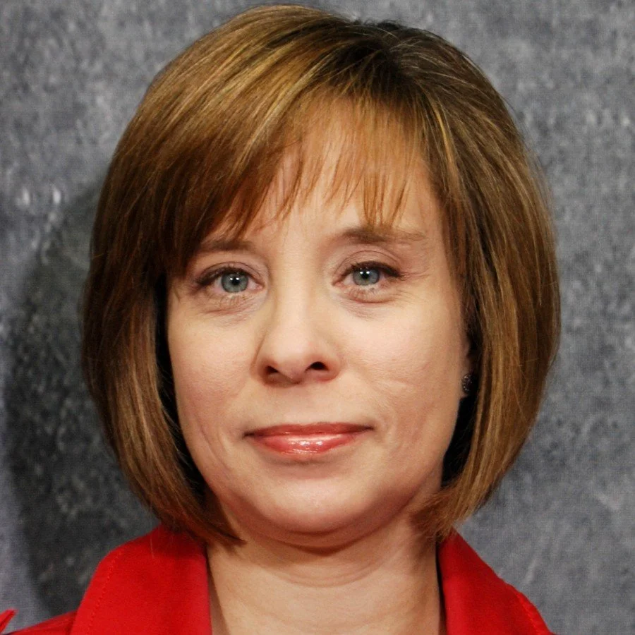White woman with short reddish blonde hair wearing a red suit
