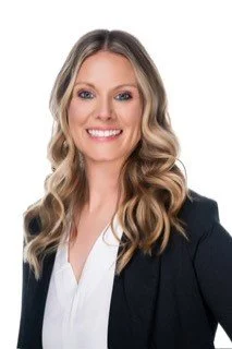 Woman with curly long blonde hair wearing a black suit jacket and white collared shirt
