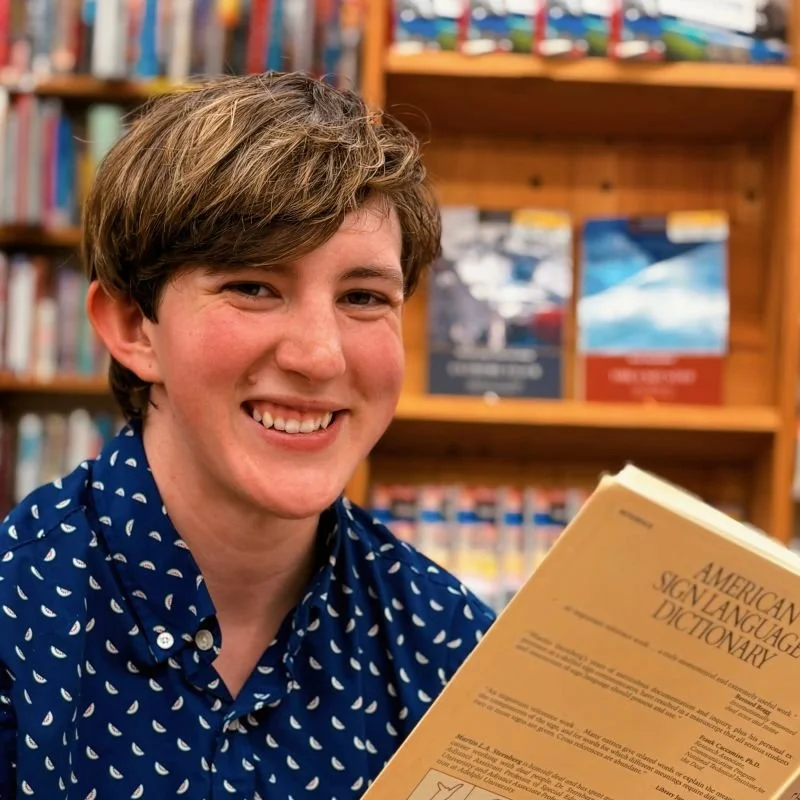 Person with short light brown hair wearing a blue and white printed collared shirt