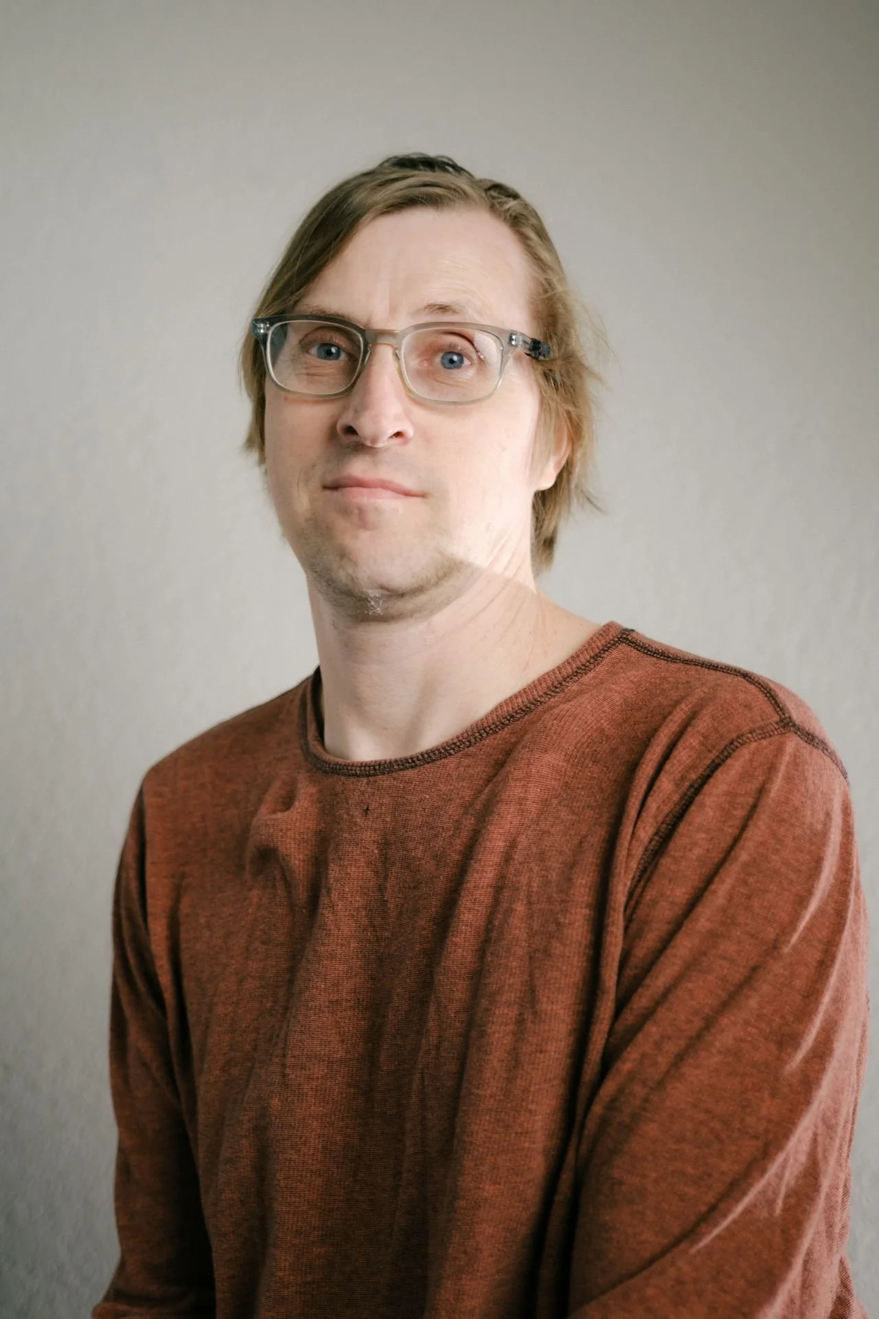 White man with short blonde hair wearing glasses and an rust orange shirt