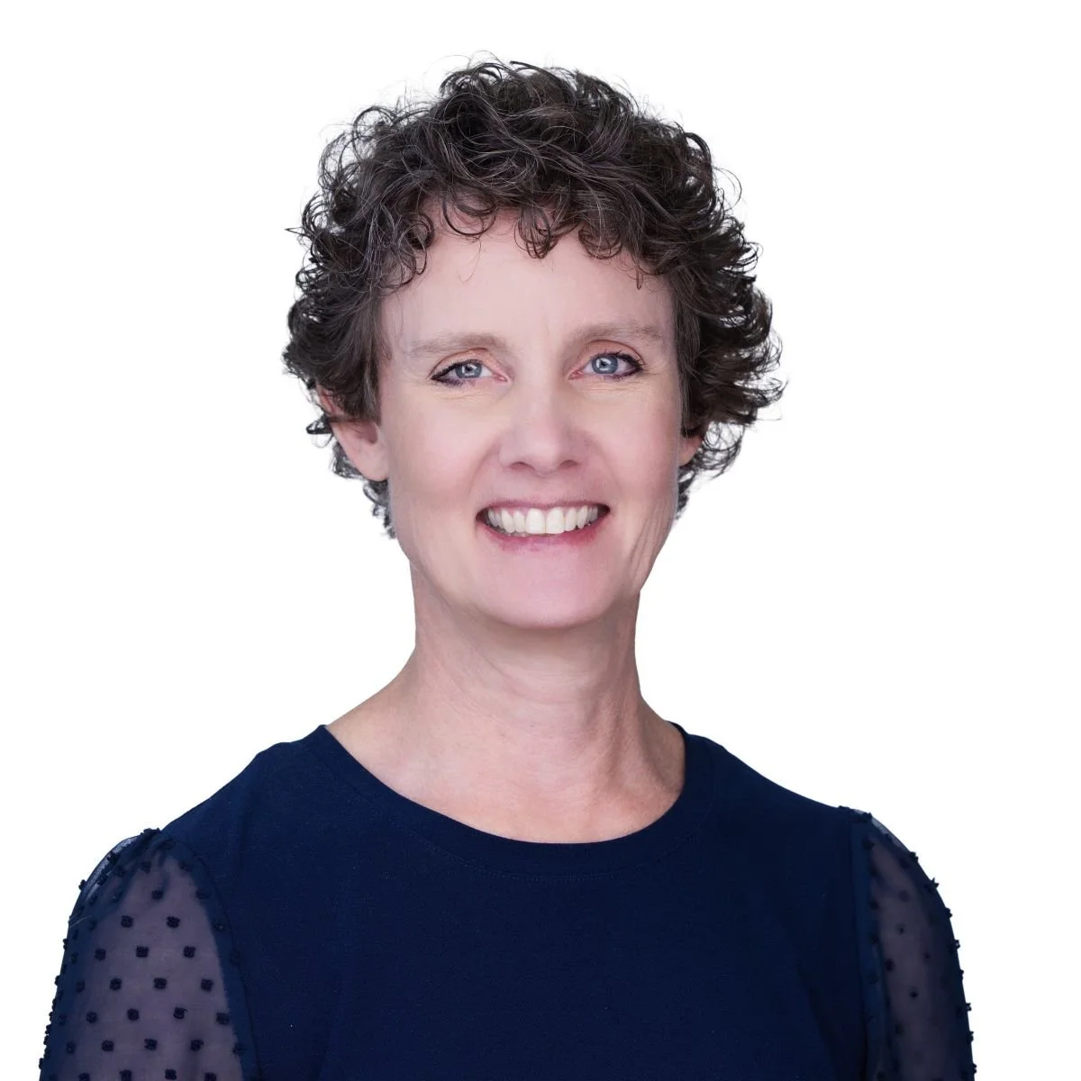 White woman with short curly red hair wearing a dark blue top