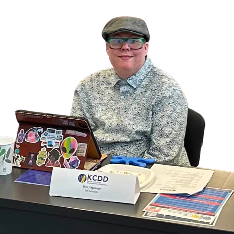 Young man wearing a cabbie hat, glasses and a floral printed shirt sitting at a table with a tablet and papers in front of him.